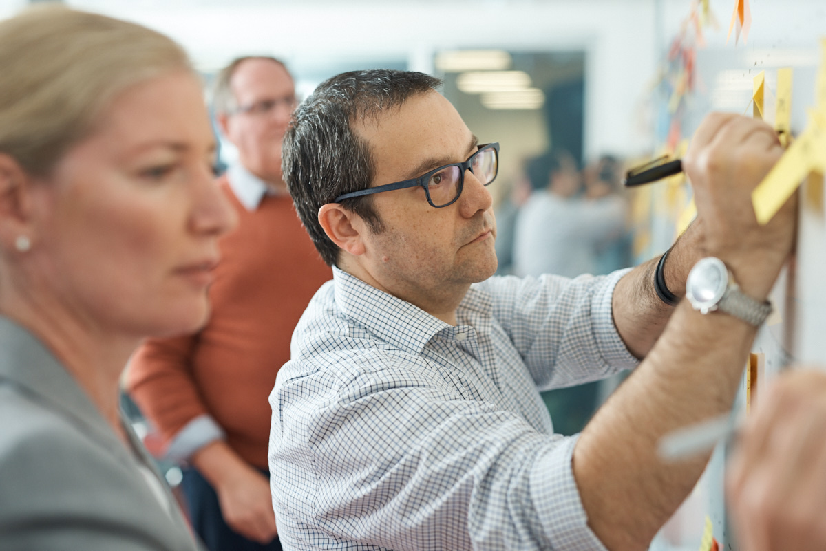 Colleagues working together at a wall of sticky notes, one writing with a marker