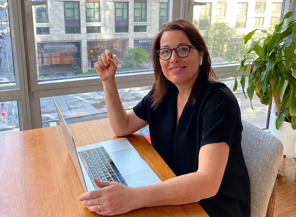 Cindy Chastain seated at a sunlit workspace by a window, laptop open